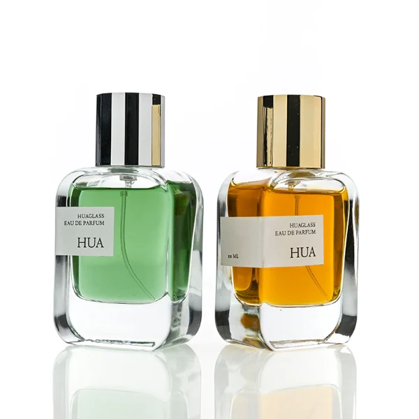 HUA0175 perfume bottle, rectangular transparent glass body with 30 ml, 50 ml, or 100 ml liquid, glossy cylindrical plastic cap in gold or silver color, printed logo label, modern minimalist luxury design, ideal for gifting and daily use.
