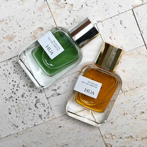 HUA0175 perfume bottle, rectangular transparent glass body with 30 ml, 50 ml, or 100 ml liquid, glossy cylindrical plastic cap in gold or silver color, printed logo label, modern minimalist luxury design, ideal for gifting and daily use.
