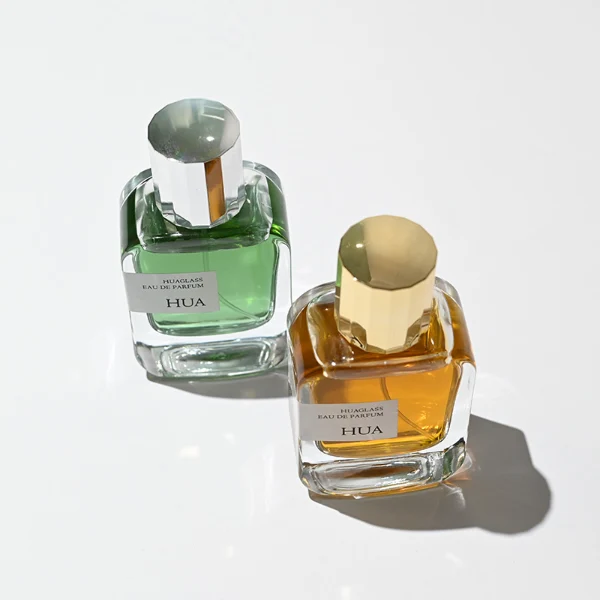 HUA0175 perfume bottle, rectangular transparent glass body with 30 ml, 50 ml, or 100 ml liquid, glossy cylindrical plastic cap in gold or silver color, printed logo label, modern minimalist luxury design, ideal for gifting and daily use.