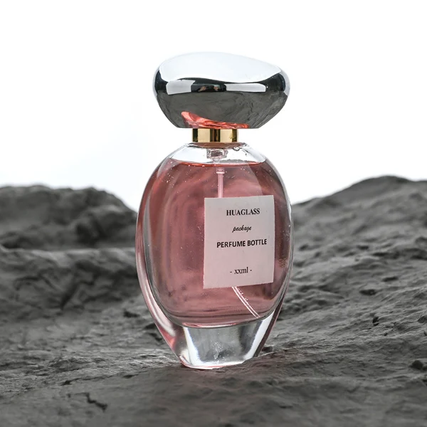 HUA0182 perfume bottle, oval transparent glass body with 30 ml, 50 ml, 75 ml, or 100 ml liquid, irregular oval-shaped glossy plastic cap with gold neck, printed logo label, modern elegant luxury design, ideal for gifting and daily use.