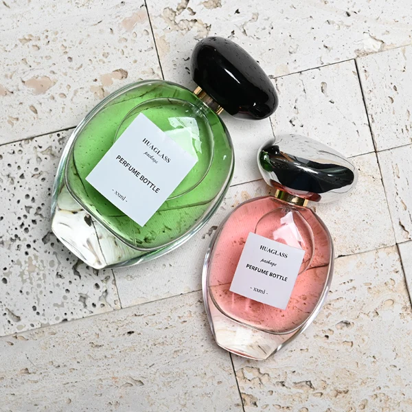 HUA0182 perfume bottle, oval transparent glass body with 30 ml, 50 ml, 75 ml, or 100 ml liquid, irregular oval-shaped glossy plastic cap with gold neck, printed logo label, modern elegant luxury design, ideal for gifting and daily use.