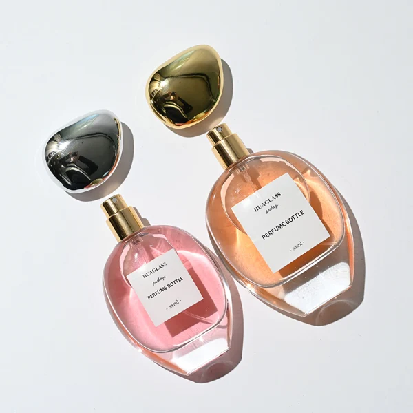 HUA0182 perfume bottle, oval transparent glass body with 30 ml, 50 ml, 75 ml, or 100 ml liquid, irregular oval-shaped glossy plastic cap with gold neck, printed logo label, modern elegant luxury design, ideal for gifting and daily use.