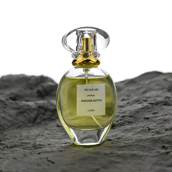 HUA0183 perfume bottle, oval transparent glass body with 30 ml, 50 ml, 75 ml, or 100 ml liquid, transparent disc-shaped plastic cap with layered decorative neck detail, printed logo label, modern elegant luxury design, ideal for gifting and daily use.