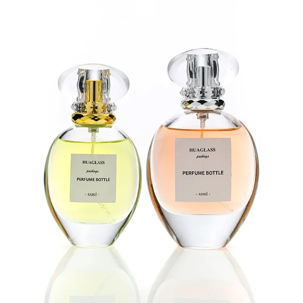 HUA0183 perfume bottle, oval transparent glass body with 30 ml, 50 ml, 75 ml, or 100 ml liquid, transparent disc-shaped plastic cap with layered decorative neck detail, printed logo label, modern elegant luxury design, ideal for gifting and daily use.