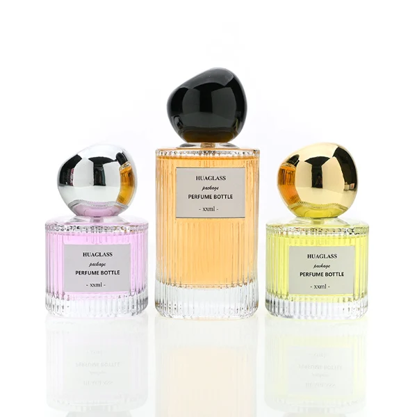 HUA0184 perfume bottle, cylindrical ribbed transparent glass body with 50 ml or 100 ml liquid, irregular glossy spherical plastic cap with customizable colors, printed logo label, modern artistic luxury design, ideal for gifting and daily use.