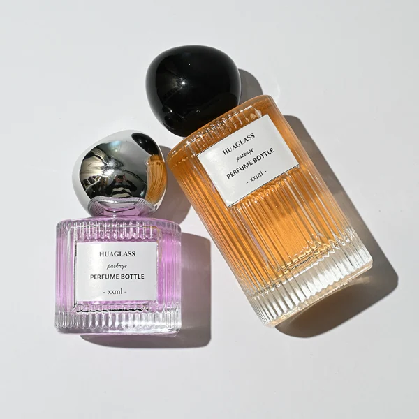 HUA0184 perfume bottle, cylindrical ribbed transparent glass body with 50 ml or 100 ml liquid, irregular glossy spherical plastic cap with customizable colors, printed logo label, modern artistic luxury design, ideal for gifting and daily use.