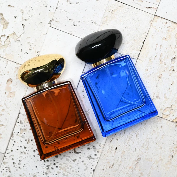 HUA0185 perfume bottle, trapezoidal transparent glass body with 50 ml or 100 ml liquid, irregular oval-shaped glossy plastic cap with customizable colors and gold neck, printed glass logo, modern fashionable luxury design, ideal for gifting and daily use.