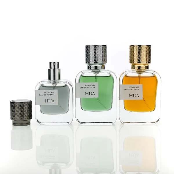HUA0186 perfume bottle, rectangular rounded transparent glass body with 30 ml, 50 ml, or 100 ml liquid, cylindrical textured Zamac cap with engraved pattern and customizable colors, printed logo label, modern premium luxury design, ideal for gifting and daily use.
