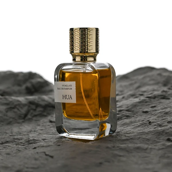 HUA0186 perfume bottle, rectangular rounded transparent glass body with 30 ml, 50 ml, or 100 ml liquid, cylindrical textured Zamac cap with engraved pattern and customizable colors, printed logo label, modern premium luxury design, ideal for gifting and daily use.