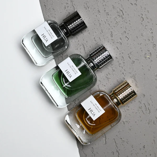 HUA0186 perfume bottle, rectangular rounded transparent glass body with 30 ml, 50 ml, or 100 ml liquid, cylindrical textured Zamac cap with engraved pattern and customizable colors, printed logo label, modern premium luxury design, ideal for gifting and daily use.
