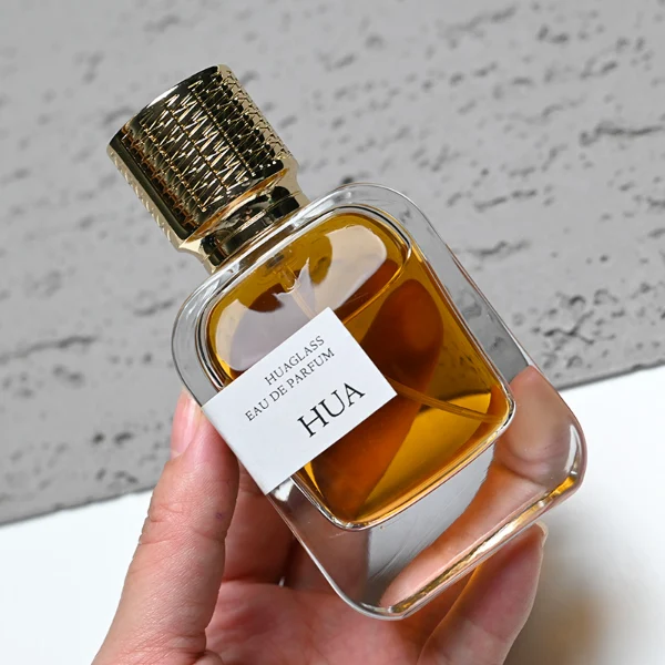 HUA0186 perfume bottle, rectangular rounded transparent glass body with 30 ml, 50 ml, or 100 ml liquid, cylindrical textured Zamac cap with engraved pattern and customizable colors, printed logo label, modern premium luxury design, ideal for gifting and daily use.