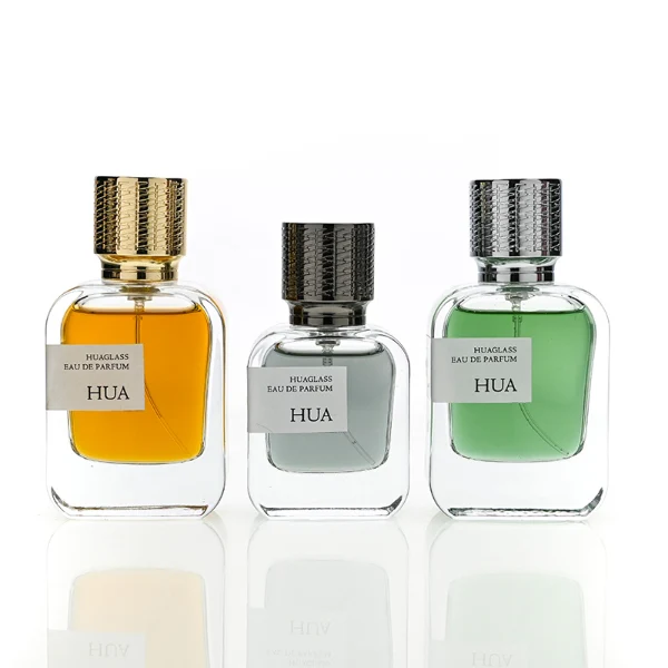 HUA0186 perfume bottle, rectangular rounded transparent glass body with 30 ml, 50 ml, or 100 ml liquid, cylindrical textured Zamac cap with engraved pattern and customizable colors, printed logo label, modern premium luxury design, ideal for gifting and daily use.