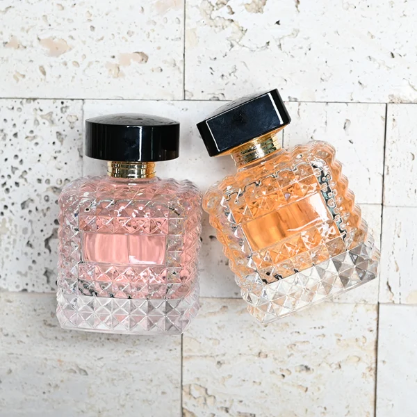 HUA0201 perfume bottle, square crystal-cut high-transparency glass body with thick base, 50 ml or 100 ml liquid, cylindrical black plastic cap with gold neck ring, brand label applied on the surface, modern luxurious design, ideal for gifting and daily use.