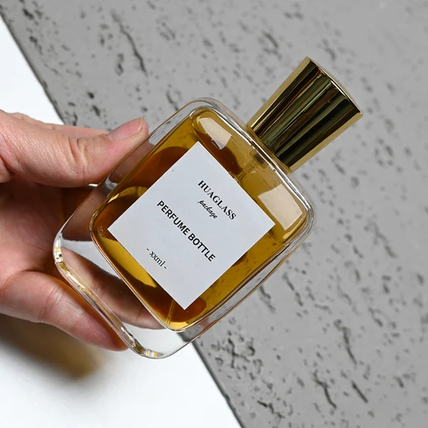 HUA0202 perfume bottle, rectangular transparent glass body with 50 ml or 100 ml liquid, stepped cylindrical plastic cap in black, gold, or silver, brand label applied on the surface, modern minimalist design, ideal for gifting and daily use.