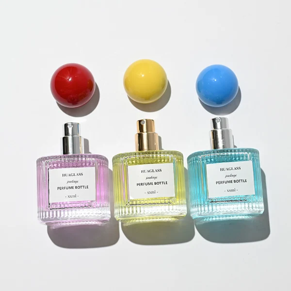 HUA0203 perfume bottle, cylindrical ribbed transparent glass body with thick base, 50 ml or 100 ml liquid, spherical glossy plastic cap in red or yellow, brand label applied on the surface, modern luxurious design, ideal for gifting and daily use.