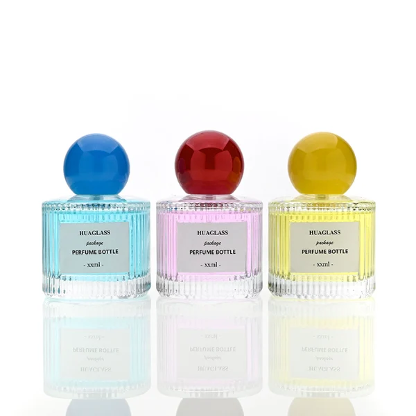 HUA0203 perfume bottle, cylindrical ribbed transparent glass body with thick base, 50 ml or 100 ml liquid, spherical glossy plastic cap in red or yellow, brand label applied on the surface, modern luxurious design, ideal for gifting and daily use.