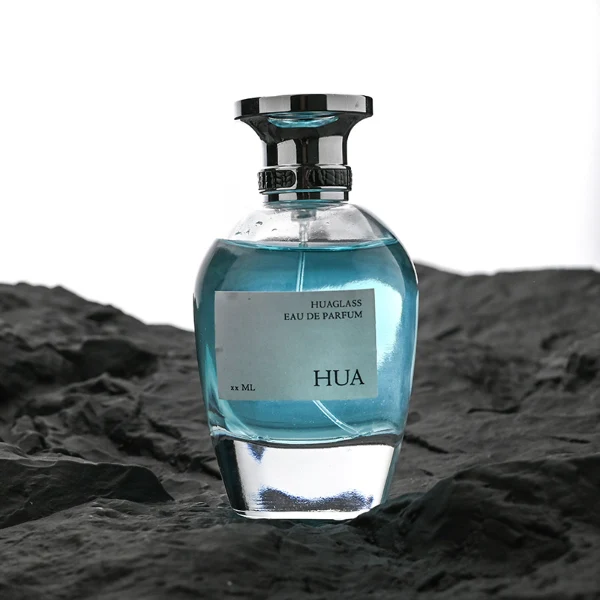 HUA0204 perfume bottle, flattened rounded streamlined transparent glass body with thick base and high-gloss finish, 100 ml liquid, flat cylindrical Zamac cap with slightly enlarged flat top fitting snugly on the neck, printed logo label, modern luxurious design, ideal for gifting and daily use.