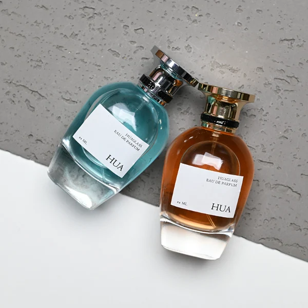 HUA0204 perfume bottle, flattened rounded streamlined transparent glass body with thick base and high-gloss finish, 100 ml liquid, flat cylindrical Zamac cap with slightly enlarged flat top fitting snugly on the neck, printed logo label, modern luxurious design, ideal for gifting and daily use.