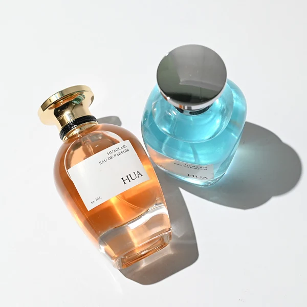 HUA0204 perfume bottle, flattened rounded streamlined transparent glass body with thick base and high-gloss finish, 100 ml liquid, flat cylindrical Zamac cap with slightly enlarged flat top fitting snugly on the neck, printed logo label, modern luxurious design, ideal for gifting and daily use.