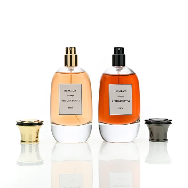 HUA0205 perfume bottle, flattened rounded streamlined transparent glass body with thick base and high-gloss finish, 100 ml liquid, flat cylindrical Zamac cap in black, gold, or silver with slightly enlarged flat top fitting snugly on the neck, brand label applied on the surface, modern luxurious design, ideal for gifting and daily use.