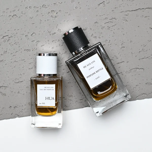 HUA0206 perfume bottle, rectangular transparent glass body with thick base, 50 ml or 100 ml liquid, cylindrical leather-wrapped cap with silver rings on both ends, brand label applied on the surface, modern masculine luxury design, ideal for gifting and daily use.