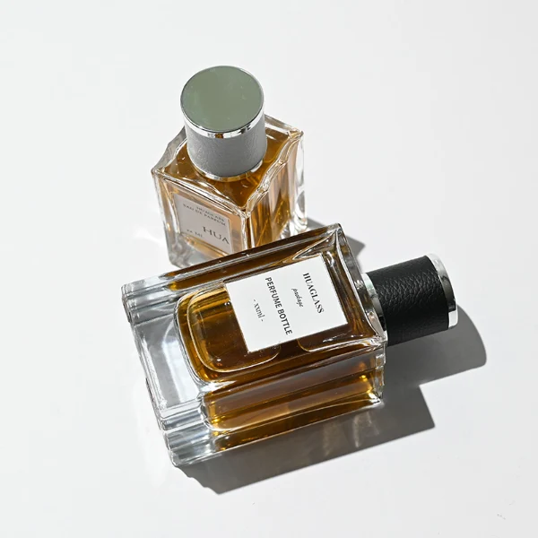 HUA0206 perfume bottle, rectangular transparent glass body with thick base, 50 ml or 100 ml liquid, cylindrical leather-wrapped cap with silver rings on both ends, brand label applied on the surface, modern masculine luxury design, ideal for gifting and daily use.