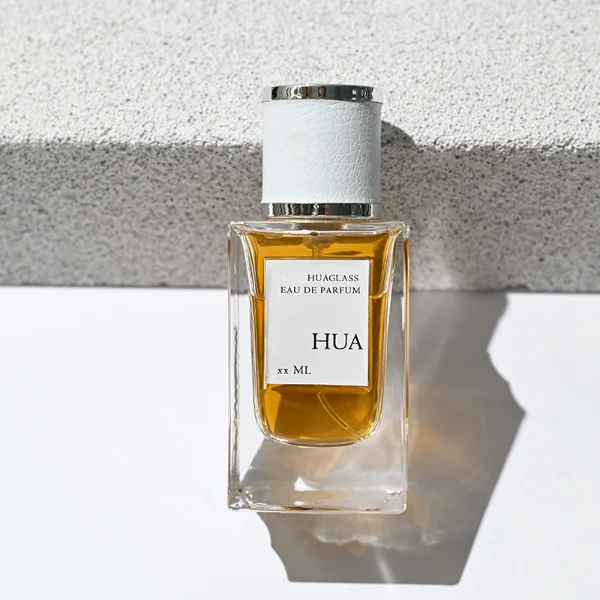 HUA0206 perfume bottle, rectangular transparent glass body with thick base, 50 ml or 100 ml liquid, cylindrical leather-wrapped cap with silver rings on both ends, brand label applied on the surface, modern masculine luxury design, ideal for gifting and daily use.