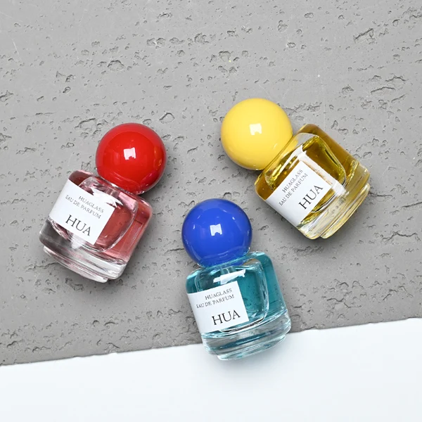 HUA0208 perfume bottle, cylindrical transparent glass body with thick base, 30 ml liquid, spherical plastic cap in blue, red, or yellow, brand label applied on the surface, modern playful luxury design, ideal for gifting and daily use.