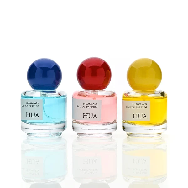 HUA0208 perfume bottle, cylindrical transparent glass body with thick base, 30 ml liquid, spherical plastic cap in blue, red, or yellow, brand label applied on the surface, modern playful luxury design, ideal for gifting and daily use.