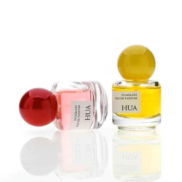 HUA0208 perfume bottle, cylindrical transparent glass body with thick base, 30 ml liquid, spherical plastic cap in blue, red, or yellow, brand label applied on the surface, modern playful luxury design, ideal for gifting and daily use.