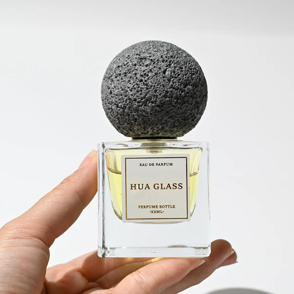 HUA0210 perfume bottle, square transparent glass body with thick base, 30 ml, 50 ml, or 100 ml liquid, spherical artificial stone cap with textured surface, brand label applied on the surface, modern artistic luxury design, ideal for gifting and daily use.