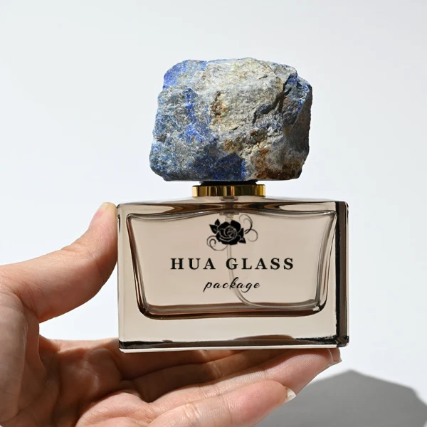 HUA0211 perfume bottle, rectangular customizable glass body with thick base, 30 ml, 50 ml, or 100 ml liquid, rough natural crystal stone cap with gold metallic neck, brand label printed on the surface, modern artistic luxury design, ideal for gifting and daily use.