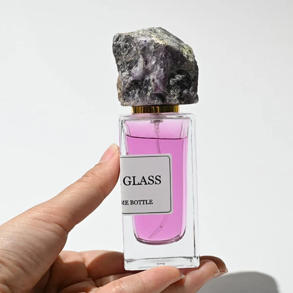 HUA0213 perfume bottle, rectangular transparent glass body with thick base, 30 ml, 50 ml, or 100 ml liquid, rough natural crystal stone cap with gold neck ring, brand label applied on the bottle surface, modern artistic luxury design, ideal for gifting and daily use.