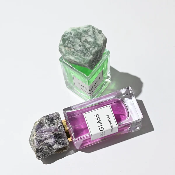 HUA0213 perfume bottle, rectangular transparent glass body with thick base, 30 ml, 50 ml, or 100 ml liquid, rough natural crystal stone cap with gold neck ring, brand label applied on the bottle surface, modern artistic luxury design, ideal for gifting and daily use.