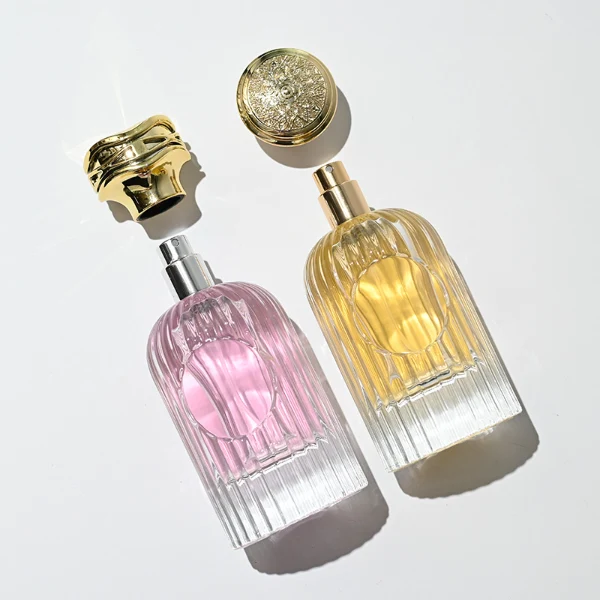 HUA0216 perfume bottle, ribbed transparent glass body with thick base, 50 ml or 100 ml liquid, cylindrical plastic cap with wave-shaped or slightly domed top with decorative grooves, metallic finish, gold logo label applied on bottle, modern luxurious fashion design, ideal for gifting and daily use.
