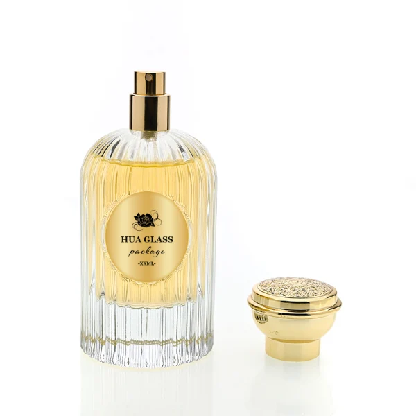 HUA0216 perfume bottle, ribbed transparent glass body with thick base, 50 ml or 100 ml liquid, cylindrical plastic cap with wave-shaped or slightly domed top with decorative grooves, metallic finish, gold logo label applied on bottle, modern luxurious fashion design, ideal for gifting and daily use.