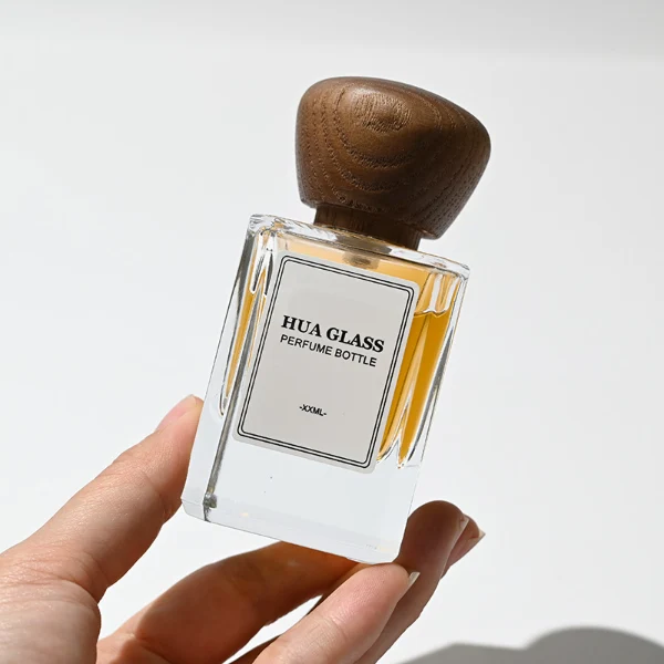 HUA0217 perfume bottle, square transparent glass body with thick base, 30 ml, 50 ml, or 100 ml liquid, rounded wooden cap, brand label applied on bottle, modern luxurious fashion design, ideal for gifting and daily use.