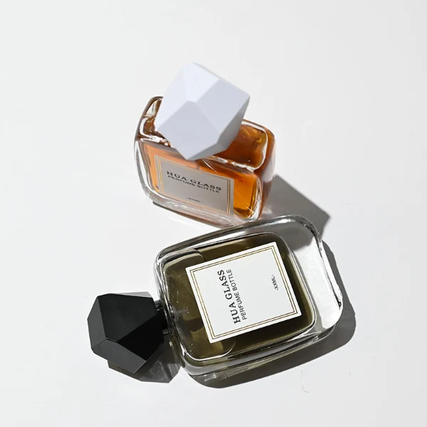 HUA0218 perfume bottle, rounded square transparent glass body with thick base, 30 ml, 50 ml, or 100 ml liquid, geometric multi-faceted plastic cap in black or white, brand label applied on bottle, modern luxurious fashion design, ideal for gifting and daily use.