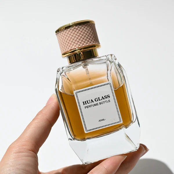 HUA0221 perfume bottle, square faceted transparent glass body with thick base, 100 ml liquid, cylindrical plastic cap wrapped with leather, textured grid pattern, gold-colored neck, brand label applied on bottle, modern luxurious fashion design, ideal for gifting and daily use.