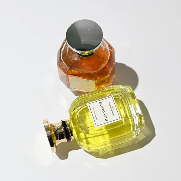 HUA0224 perfume bottle, multifaceted transparent glass body with thick base, 100 ml liquid, cylindrical plastic cap with slightly flared flat top and gold or silver neck ring, brand label applied on bottle, modern luxurious fashion design, ideal for gifting and daily use.