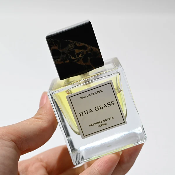 HUA0226 perfume bottle, square transparent glass body with thick base, 30 ml, 50 ml, or 100 ml liquid, square natural stone cap with customizable color and organic stone texture, brand label applied on bottle, modern luxurious fashion design, ideal for gifting and daily use.