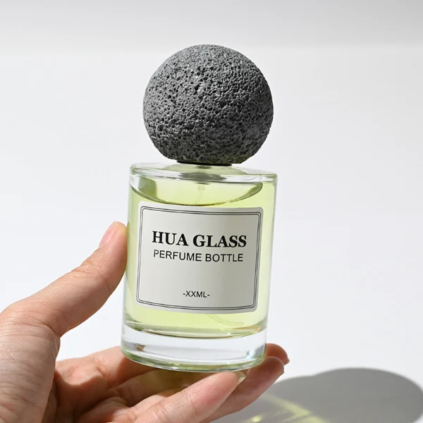 HUA0228 perfume bottle, cylindrical transparent glass body with thick base, 30 ml, 50 ml, or 100 ml liquid, spherical artificial stone cap with natural texture, brand label applied on bottle, modern luxurious fashion design, ideal for gifting and daily use.