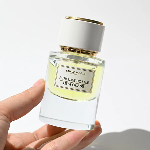 HUA0242 perfume bottle, cylindrical transparent glass body with thick base, 30 ml, 50 ml, or 100 ml liquid, cylindrical plastic cap with black or white side and silver plastic rings on both top and bottom, brand label applied on bottle, modern luxurious design, ideal for gifting and daily use.