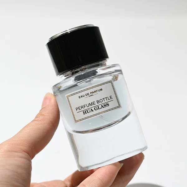 HUA0242 perfume bottle, cylindrical transparent glass body with thick base, 30 ml, 50 ml, or 100 ml liquid, cylindrical plastic cap with black or white side and silver plastic rings on both top and bottom, brand label applied on bottle, modern luxurious design, ideal for gifting and daily use.