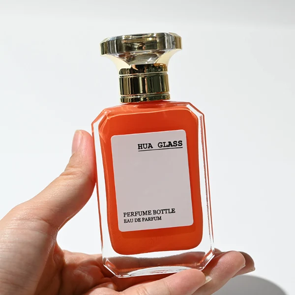 HUA0245 perfume bottle, rectangular transparent glass body with beveled corners and thick base, customizable inner spray colors, 30 ml, 50 ml, or 100 ml liquid, irregular metallic plastic cap with silver or gold side bar details, printed logo label, modern luxury fashion design, ideal for gifting and daily use.