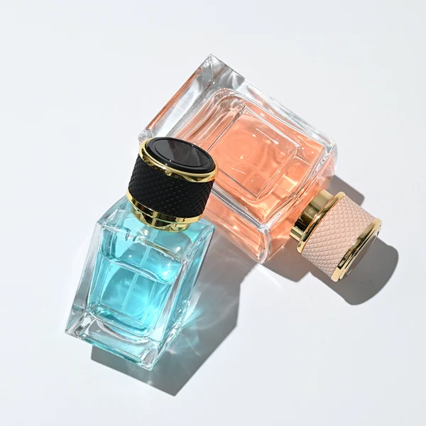 HUA0248 perfume bottle, rectangular transparent glass body with thick base, 50 ml or 100 ml liquid, cylindrical plastic cap wrapped with leather, gold-colored bottle neck, brand label applied on bottle, modern luxurious design, ideal for gifting and daily use.