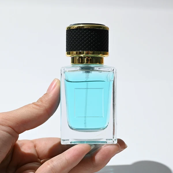 HUA0248 perfume bottle, rectangular transparent glass body with thick base, 50 ml or 100 ml liquid, cylindrical plastic cap wrapped with leather, gold-colored bottle neck, brand label applied on bottle, modern luxurious design, ideal for gifting and daily use.