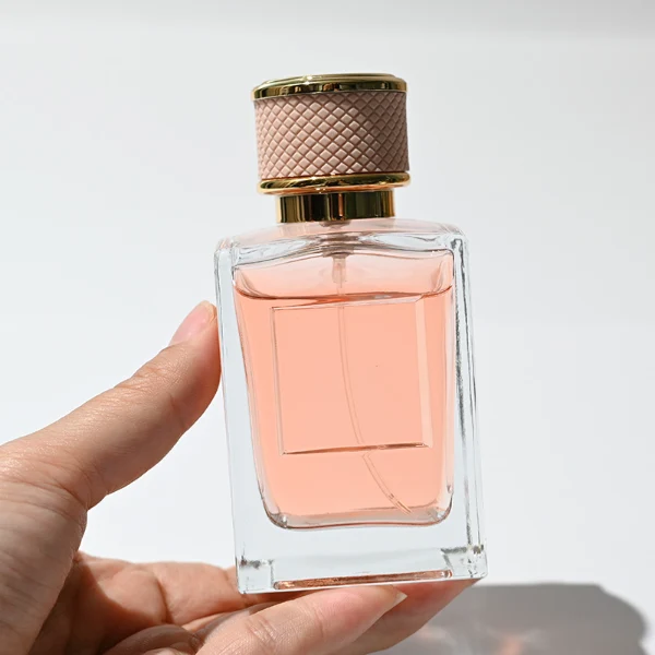 HUA0248 perfume bottle, rectangular transparent glass body with thick base, 50 ml or 100 ml liquid, cylindrical plastic cap wrapped with leather, gold-colored bottle neck, brand label applied on bottle, modern luxurious design, ideal for gifting and daily use.