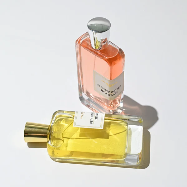 HUA0251 perfume bottle, rectangular transparent glass body with thick base, 100 ml liquid, cylindrical plastic cap with smooth high-gloss surface, flat top, straight uniform sides, tightly fitted to bottle neck, brand label applied on bottle, modern luxurious design, ideal for gifting and daily use.