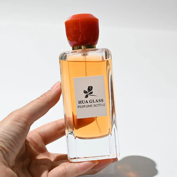 HUA0252 perfume bottle, rectangular transparent glass body with rounded edges and thick base, 50 ml or 80 ml liquid, yellow or red faceted geometric resin cap with smooth glossy finish, gold-colored bottle neck, brand label applied on bottle, modern artistic luxury design, ideal for gifting and daily use.